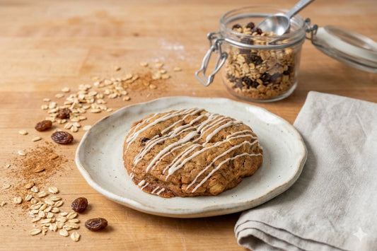 The Sunflour Baking Company Oatmeal Golden Raisin Cookie with white icing on a plate, oats, raisins, and granola jar in the background.