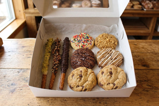 An Ohhhh Zone Cookie & Pretzel Box by Sunflour Baking Company sits open on a wooden table, filled with treats.