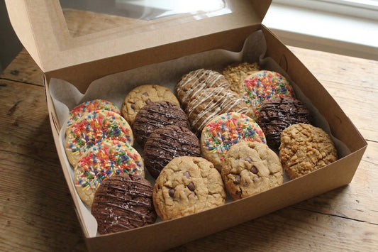 The Comfort Zone Cookie Box by Sunflour Baking Company features fresh chocolate chip, oatmeal, and sprinkle cookies on parchment paper.