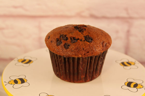 A chocolate chip muffin made with Sunflour Baking Company Banana Muffin Mix sits on a plate with cartoon bees, ready to bake at home.