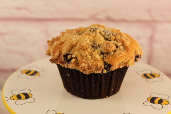 A blueberry muffin made from Sunflour Baking Company Blueberry Muffin Mix sits on a plate with cartoon bees and flowers.