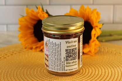 A Classic Birthday Cake Jar by Sunflour Baking Company with a gold lid sits on a yellow mat, sunflowers behind, QR code on label.