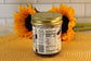 A glass jar of Sunflour Baking Company Cookies and Cream with a gold lid sits on a mat, in front of two sunflowers.