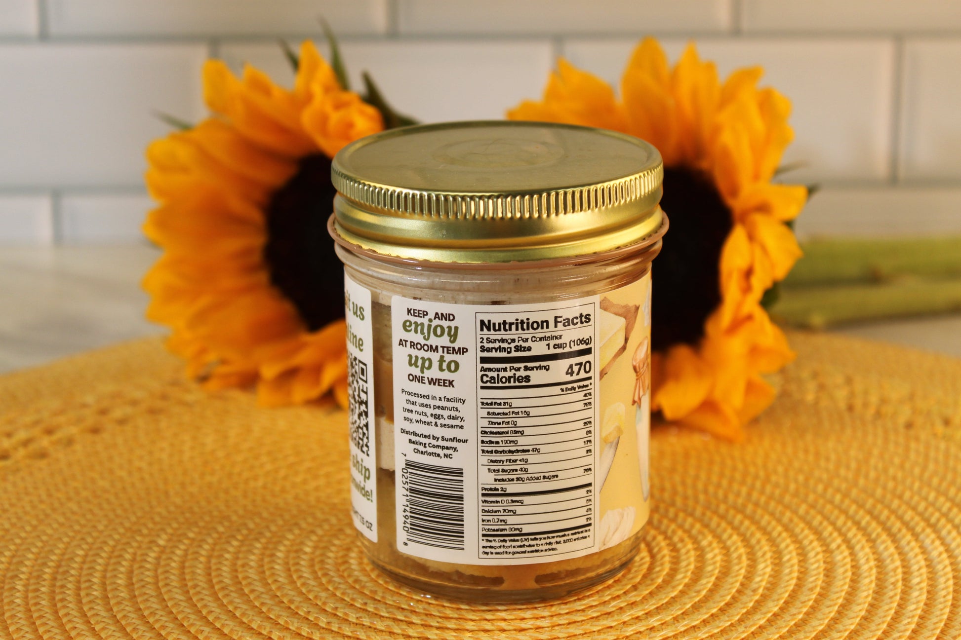 A French Toast jar from Sunflour Baking Company with nutrition facts, in front of two sunflowers on a yellow surface.