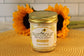 A Sunflour Baking Company Lemon Drop Cake in a Jar sits on a yellow mat, sunflowers in the background.