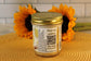 A jar of Lemon Drop by Sunflour Baking Company with a gold lid and QR code sits on a woven mat, sunflowers behind.