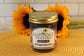 A jar of Sunflour Baking Company Midnight Chocolate Cake in a Jar rests on a woven mat, sunflowers in the background.