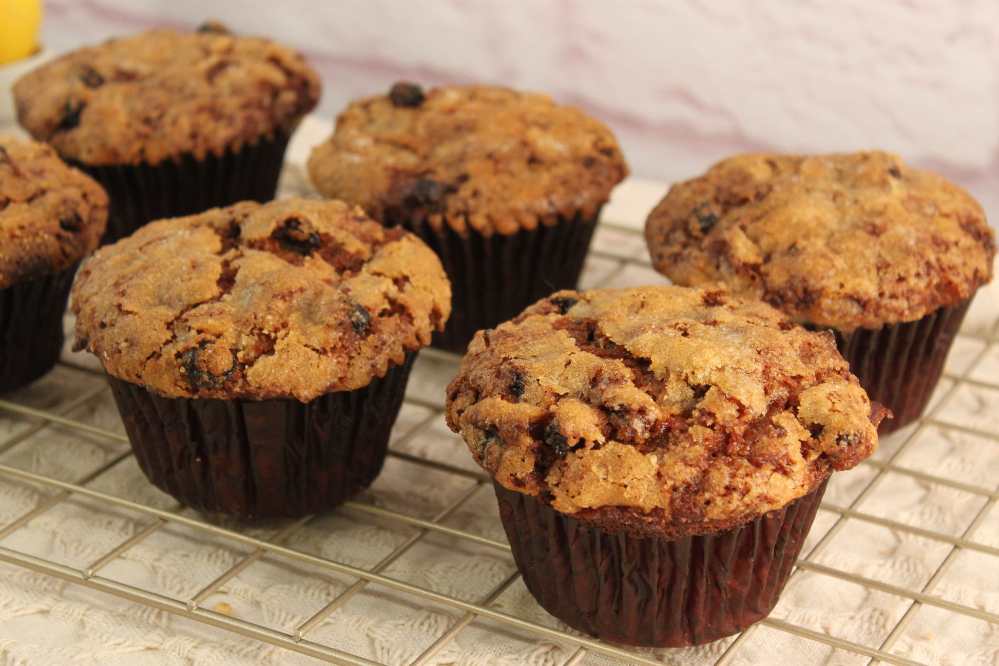 Six Morning Glory Muffins from Sunflour Baking Company cool on a wire rack, each in a dark paper liner.