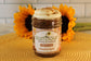 A Pumpkin Spice jar from Sunflour Baking Company sits on a yellow mat with sunflowers in the background.