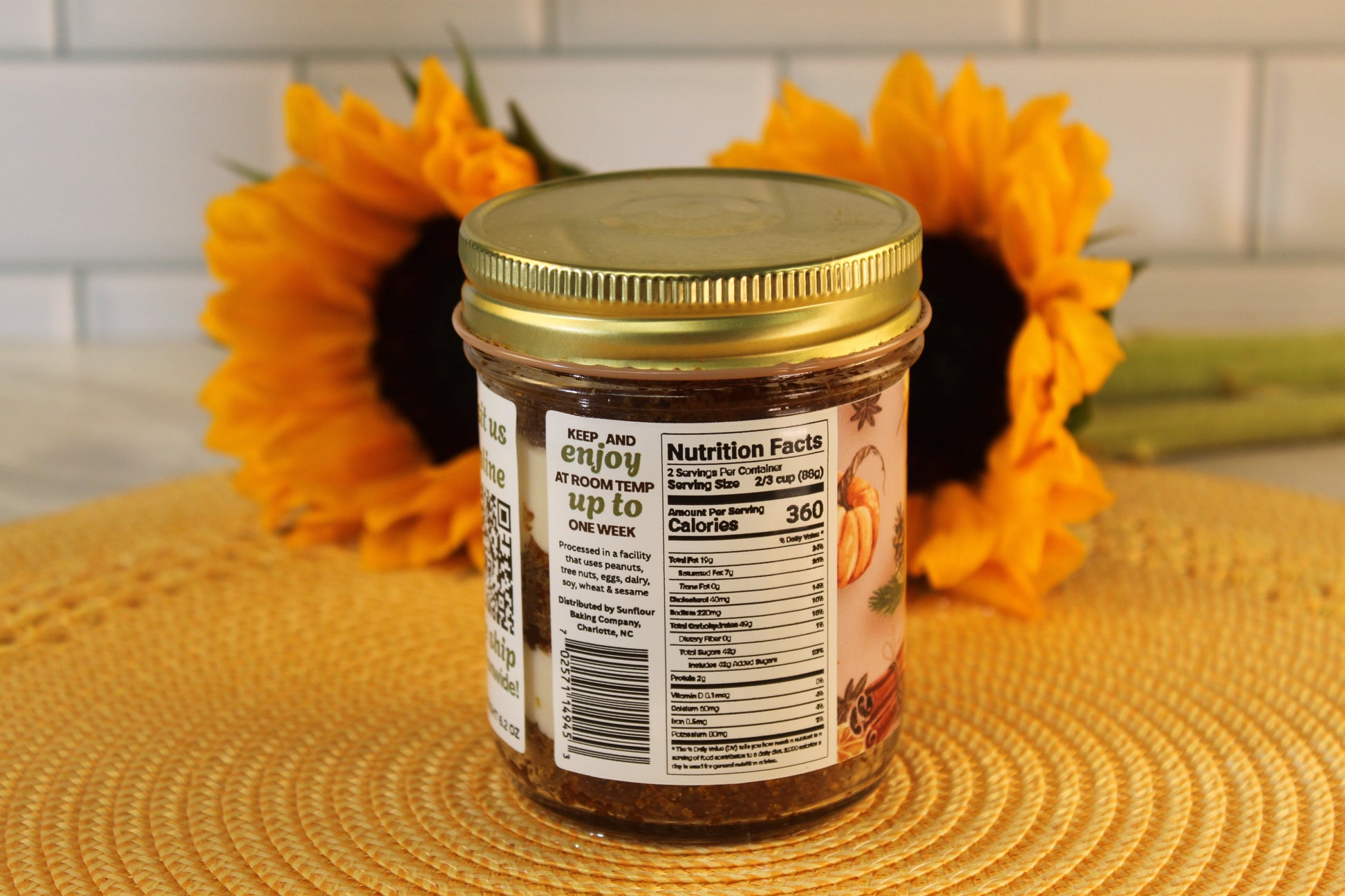 Sunflour Baking Company Pumpkin Spice Cake Jar with gold lid and nutrition facts, set before two sunflowers on a white surface.