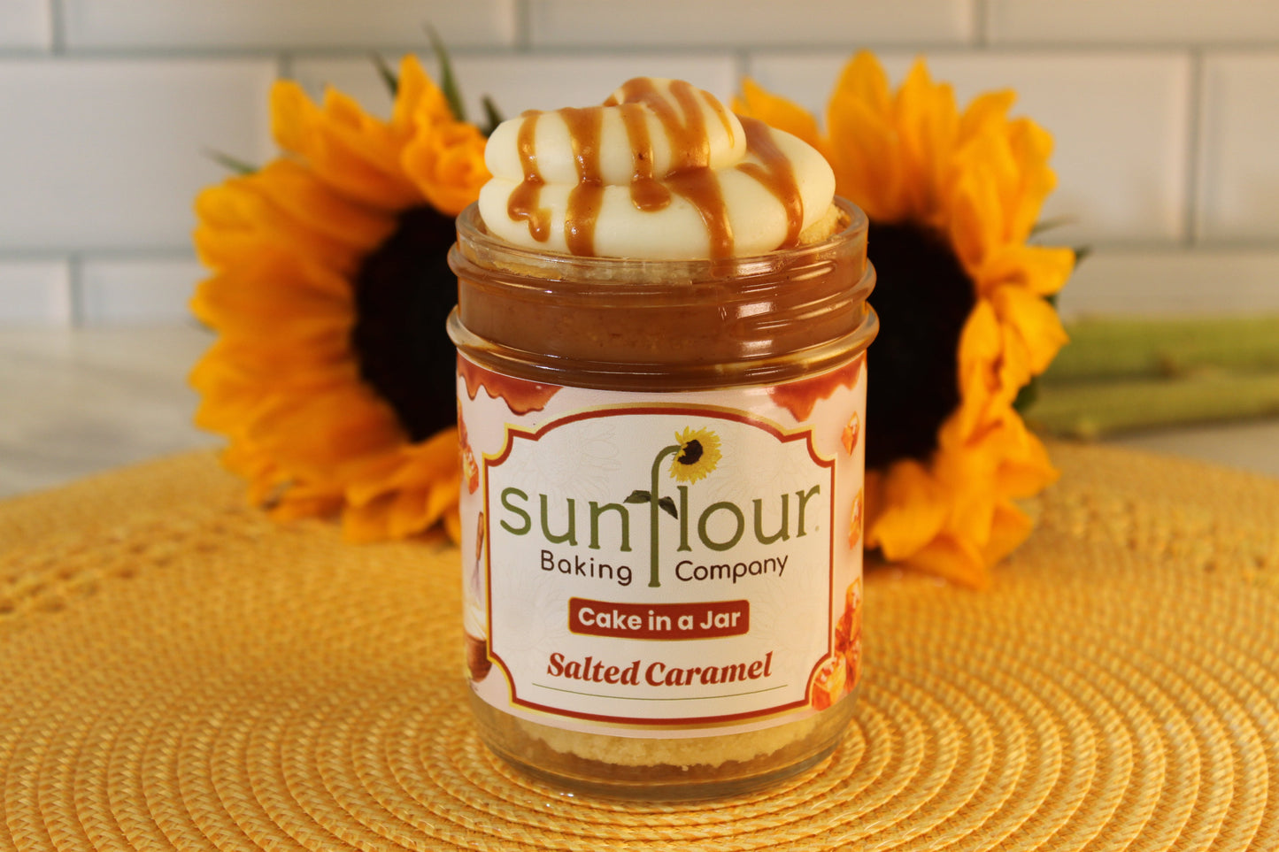 A Salted Caramel jar from Sunflour Baking Company rests on a yellow mat with sunflowers in the background.