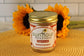 A Sunflour Baking Company Salted Caramel cake jar, pictured with sunflowers and a woven mat in the background.