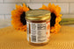 A Salted Caramel jar by Sunflour Baking Company with a gold lid sits on a mat, two sunflowers in the background.