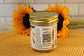 A VGF Blondie by Sunflour Baking Company in a glass jar with gold lid sits on a yellow placemat with two sunflowers behind.