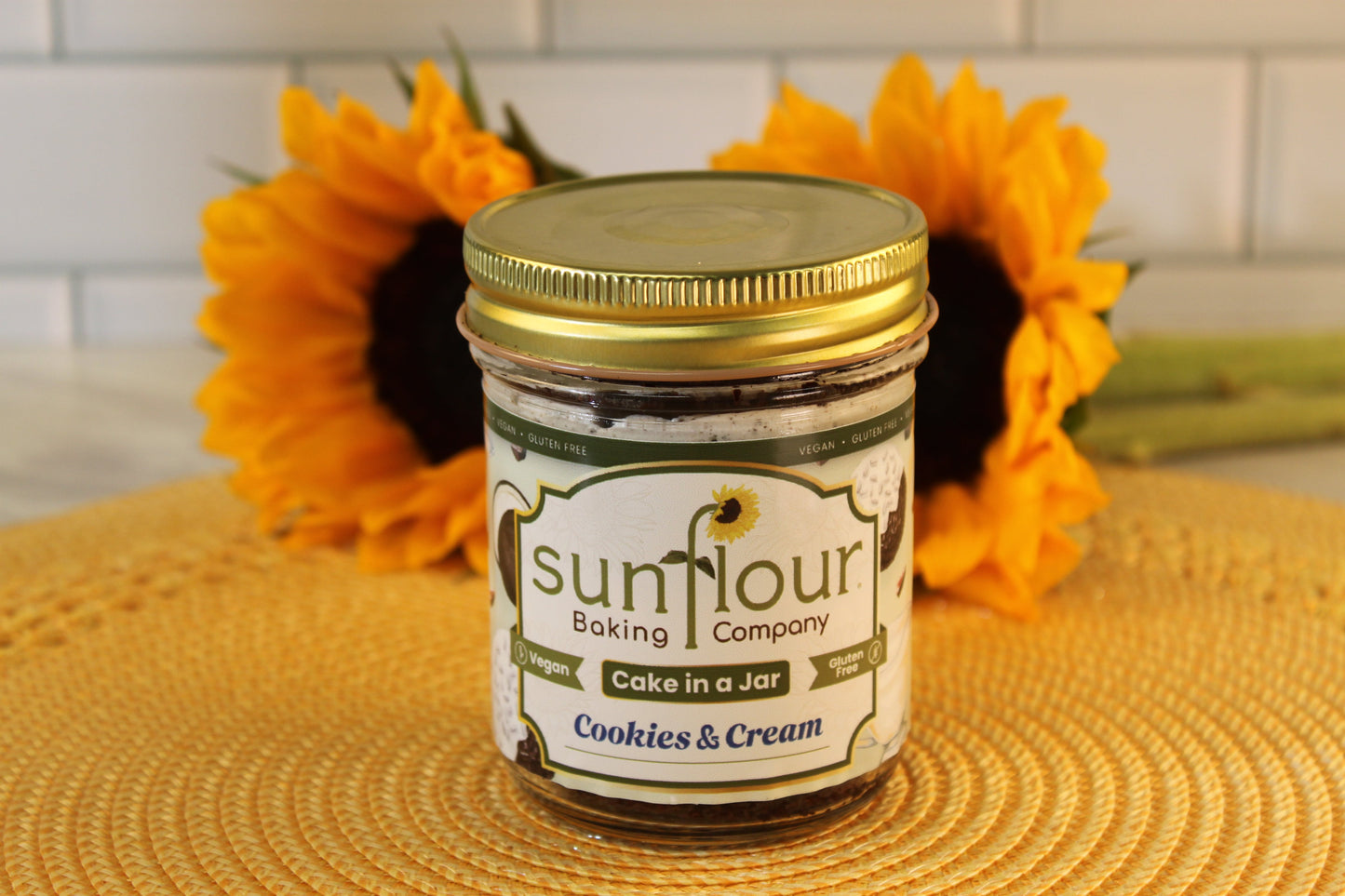 A jar labeled Sunflour Baking Company VGF Cookies and Cream is displayed in front of two sunflowers.
