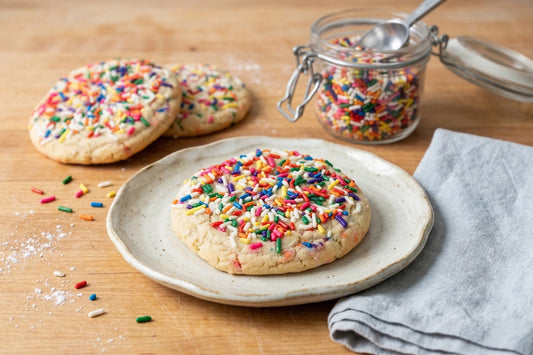 The Rainbow Sprinkle Cookie by Sunflour Baking Company is a large sugar cookie topped with colorful sprinkles.