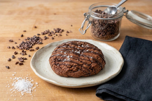 The Midnight Chocolate Cookie by Sunflour Baking Company is drizzled with chocolate and sea salt, served on a wooden surface.