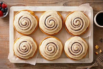 Six fresh-baked Sunflour Baking Company Cinnamon Rolls with white icing, served with coffee and berries—great for gifting.
