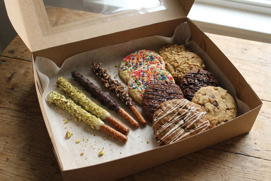 Ohhhh Zone Cookie & Pretzel Box by Sunflour Baking Company on wood table with assorted cookies and chocolate-covered pretzels.