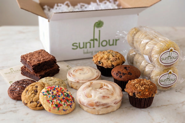 A Sunflour Baking Company Bakery Gift Basket with sourdough English muffins and gourmet cookies displayed on a table.